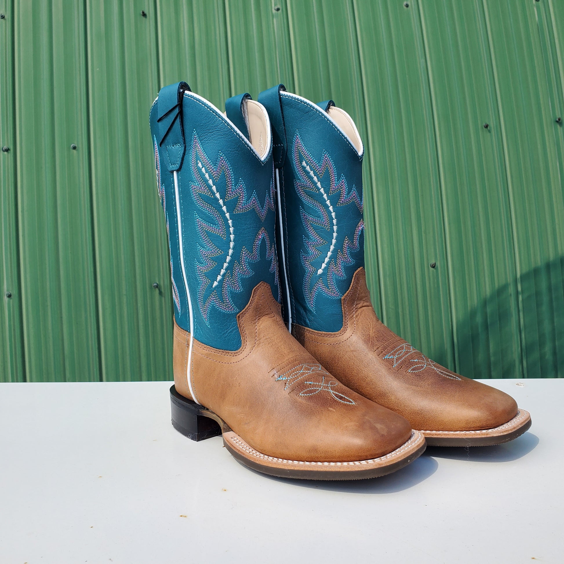 A pair of children's boots with a teal upper and tan leather foot, featuring a rubberized outsole and horseman heel.