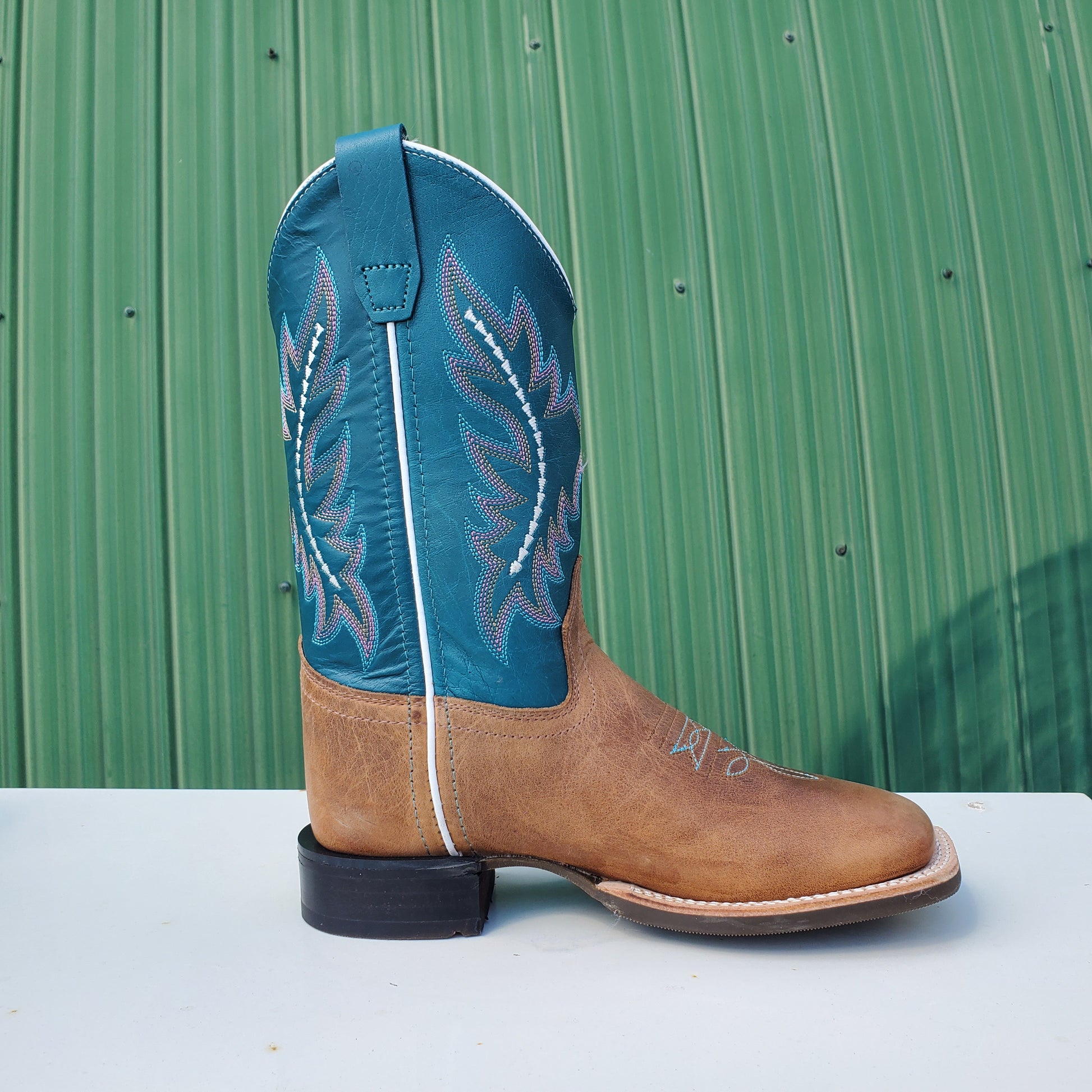 a kids boot with a teal upper and tan leather foot, featuring a rubberized outsole and horseman heel.
