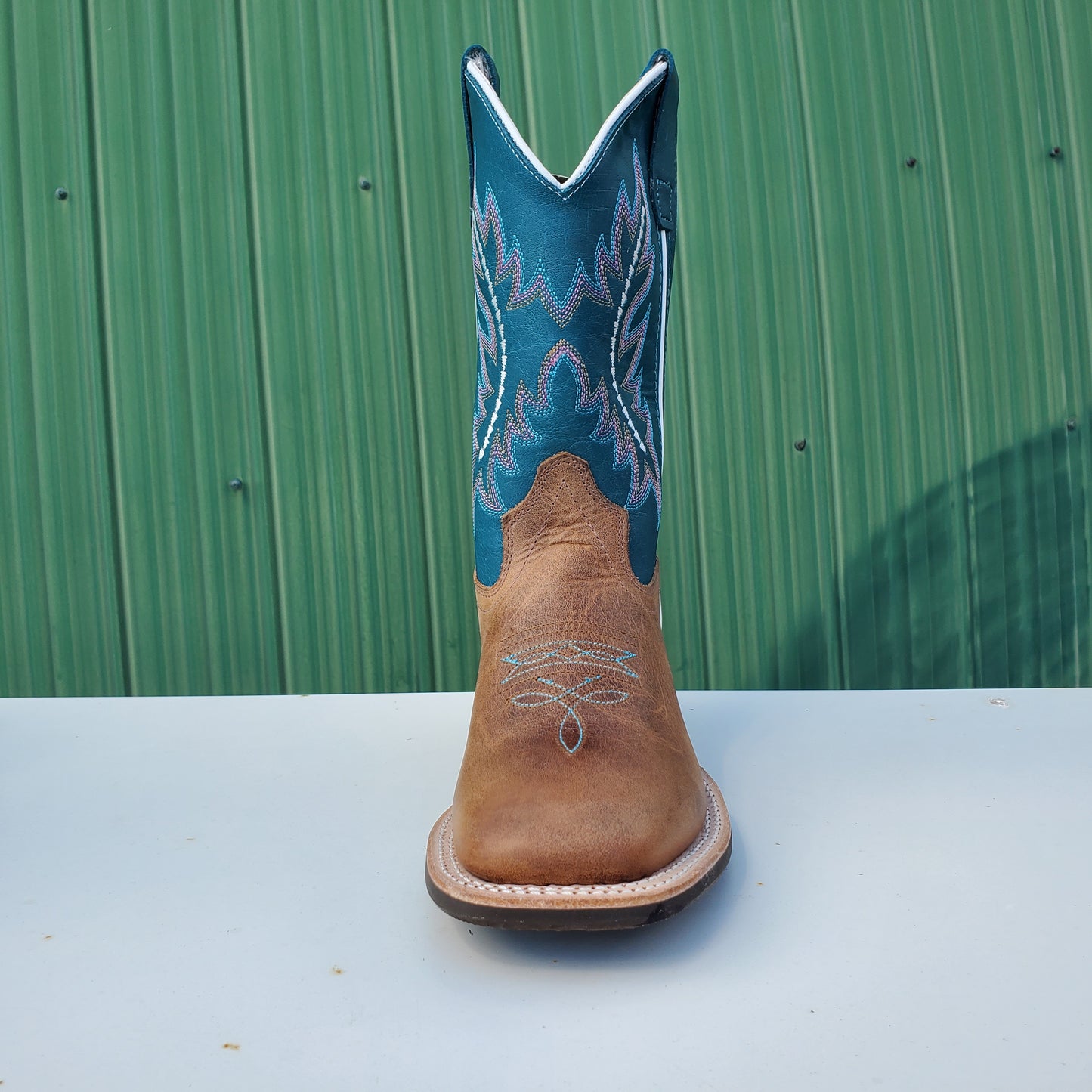 a kids boot with a teal upper and tan leather foot, featuring a rubberized outsole and horseman heel.