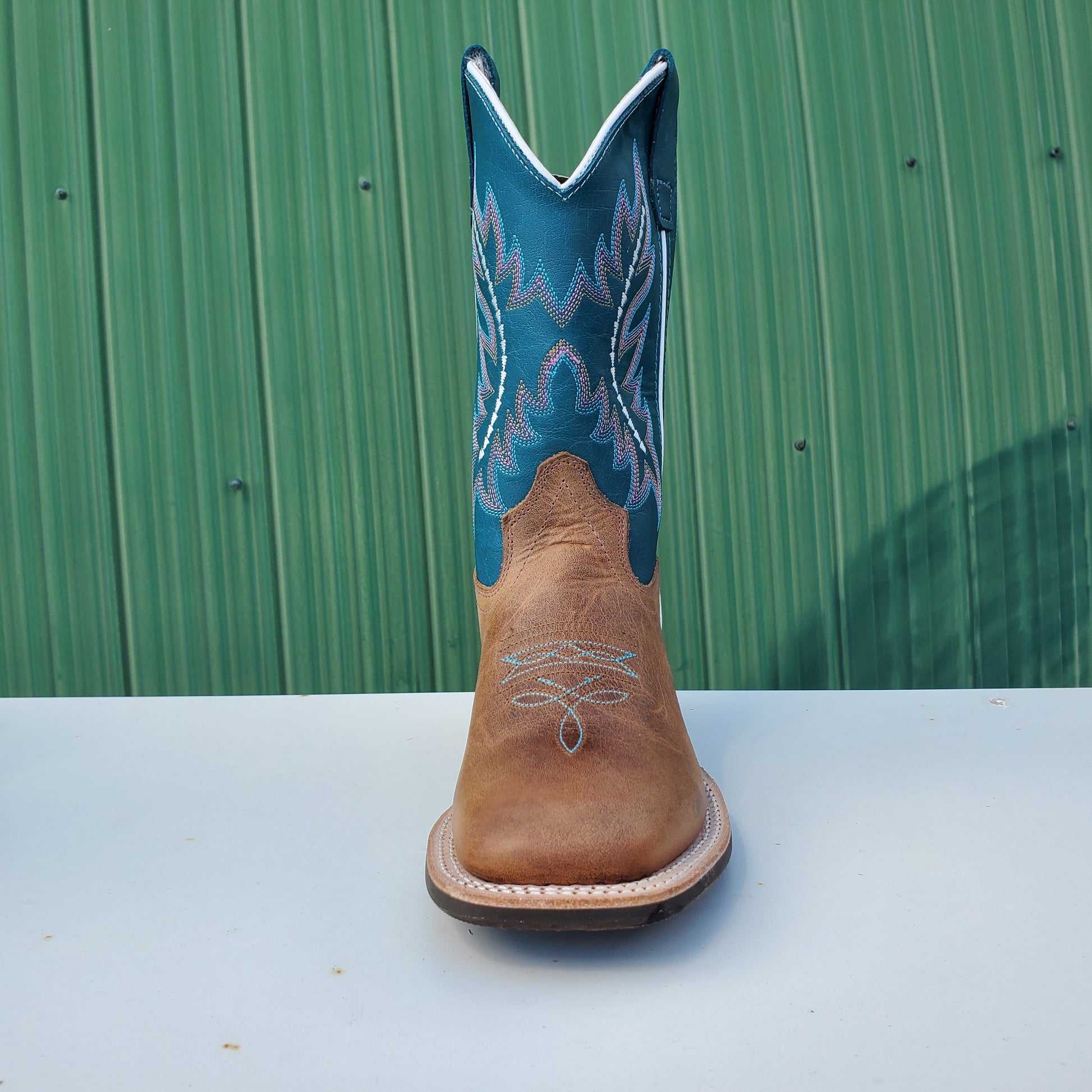 a kids boot with a teal upper and tan leather foot, featuring a rubberized outsole and horseman heel.