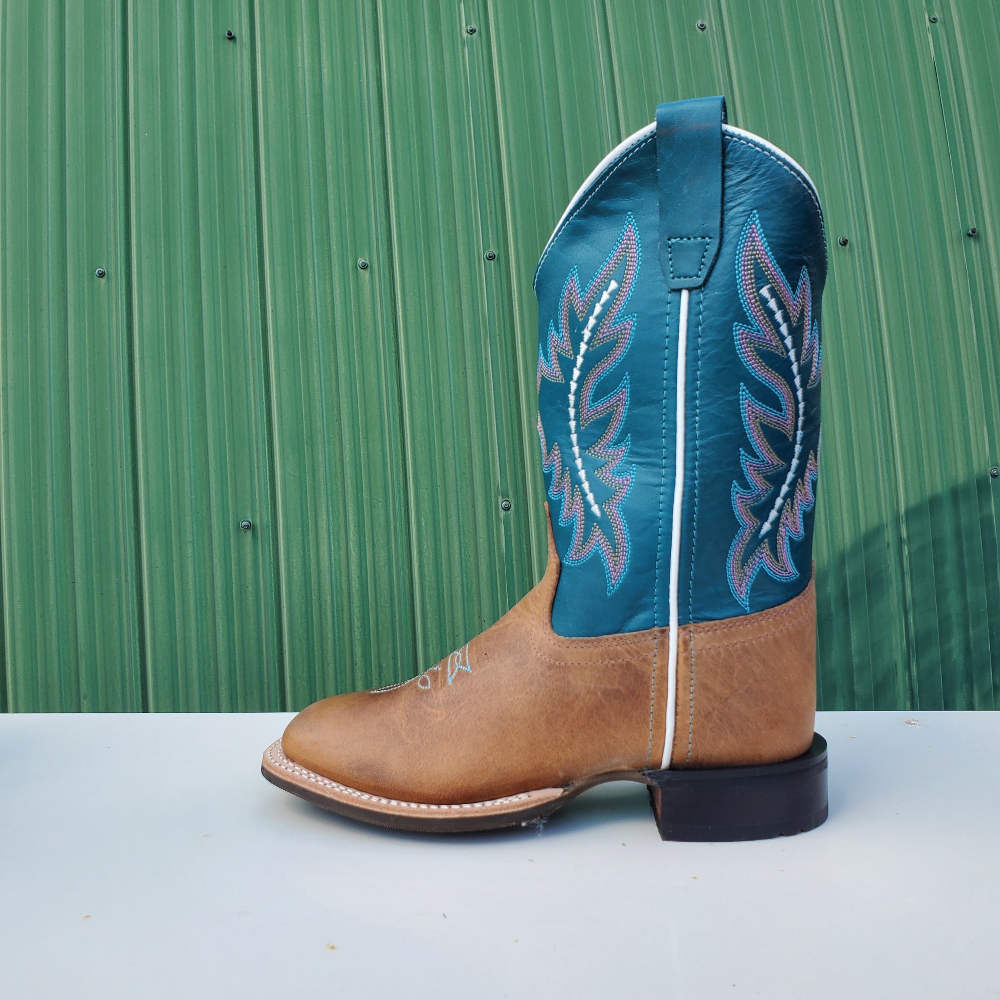 a kids boot with a teal upper and tan leather foot, featuring a rubberized outsole and horseman heel.