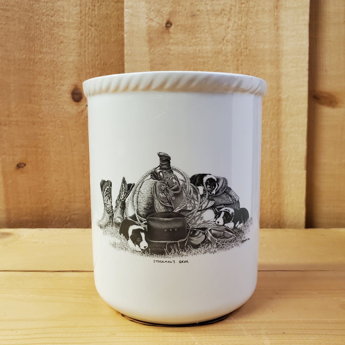 a white ceramic utensil holder with western pencil art featuring puppies on a western saddle