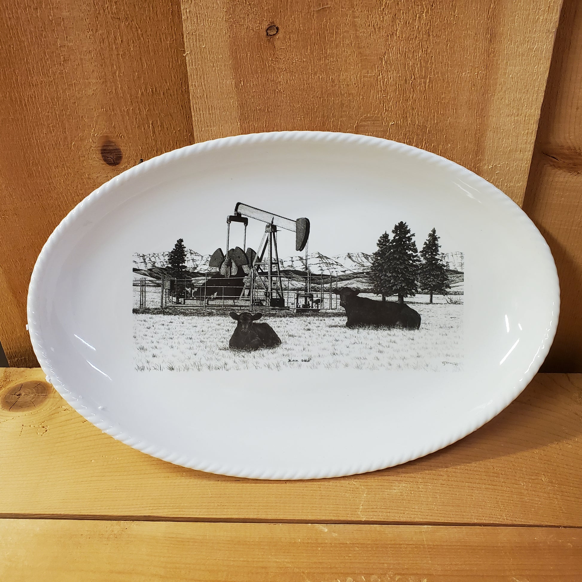 A white serving platter with a printed illustration featuring black cows and an oil pump