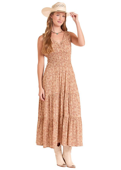 A woman modeling a sleeveless, tiered maxi dress with a warm beige and brown floral pattern, paired with a straw cowboy hat and light-colored boots, set against a plain white background.