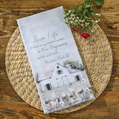 A kitchen towel that says 'Farm Life' on a woven mat with flowers on a wooden surface