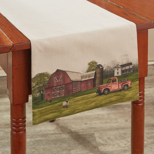 Table runner with a farm scene featuring a red barn and rusty truck on a wooden table.