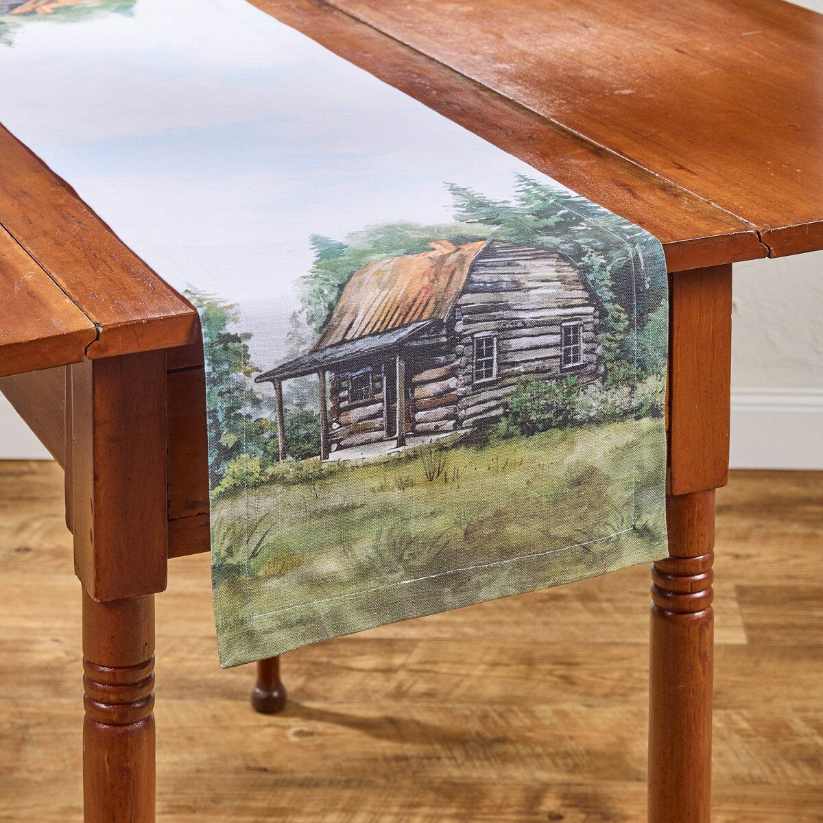 Wooden table with a scenic table runner featuring a log cabin.