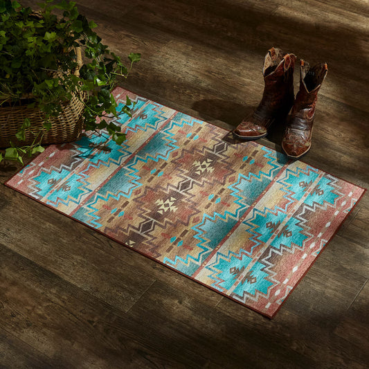 Patterned rug with cowboy boots on a wooden floor next to a plant