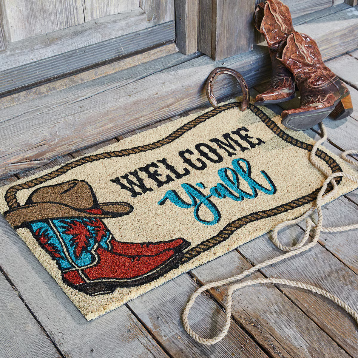 Doormat with cowboy boot and hat design, featuring the text 'Welcome Y'all', placed on a wooden floor.