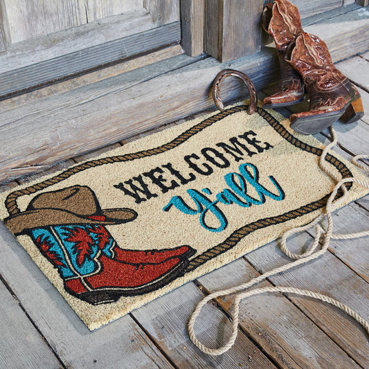 Doormat with cowboy boot and hat design, featuring the text 'Welcome Y'all', placed on a wooden floor.