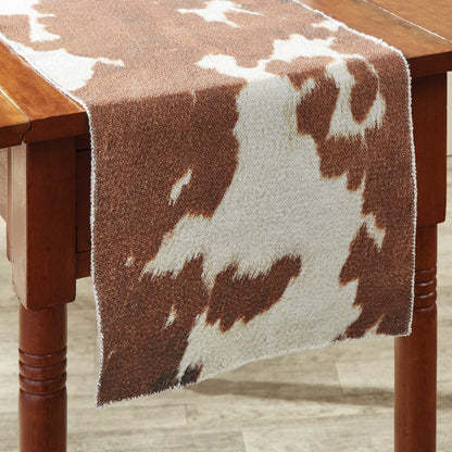 Brown and white cowhide patterned table runner on a wooden table.