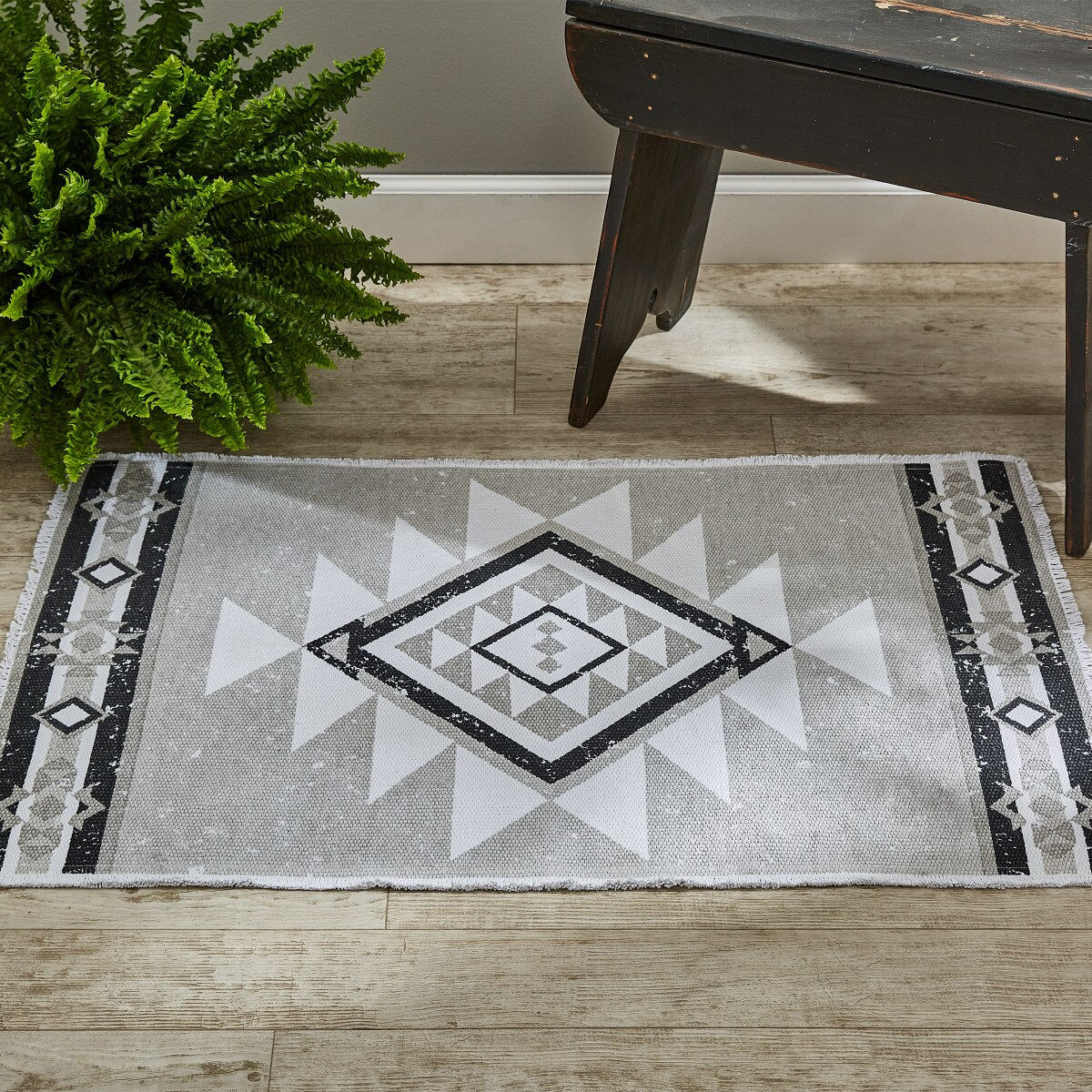 Geometric patterned rug on a wooden floor with a plant and dark wooden furniture.