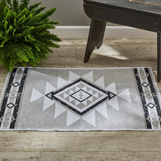 Geometric patterned rug on a wooden floor with a plant and dark wooden furniture.