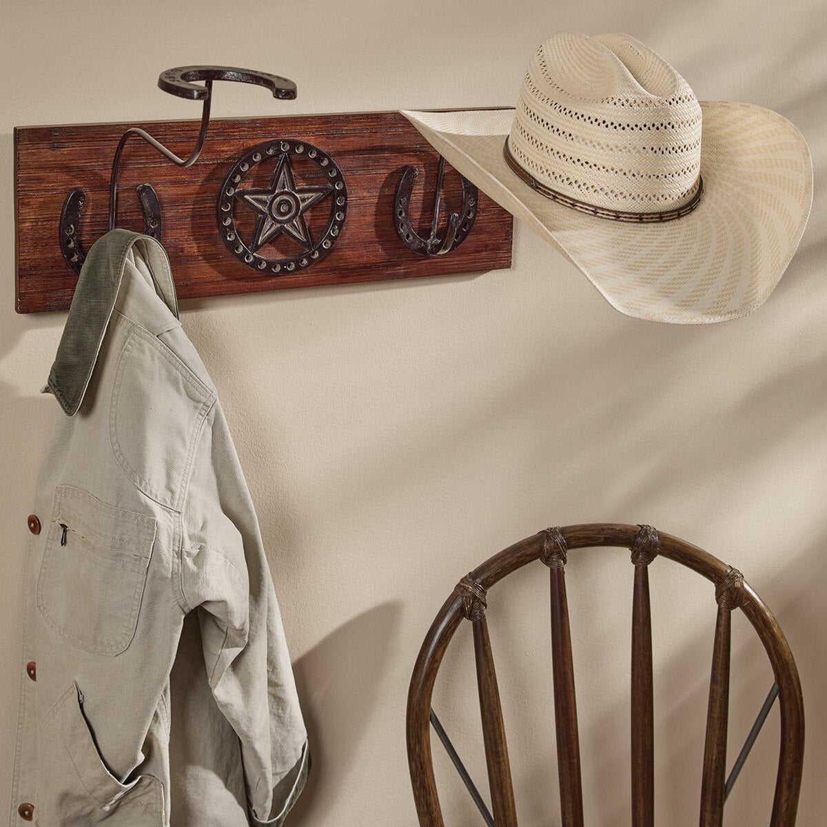 Wooden wall hook with star and horseshoe design, hat, and jacket on a beige wall.