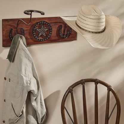 Wooden wall hook with star and horseshoe design, hat, and jacket on a beige wall.