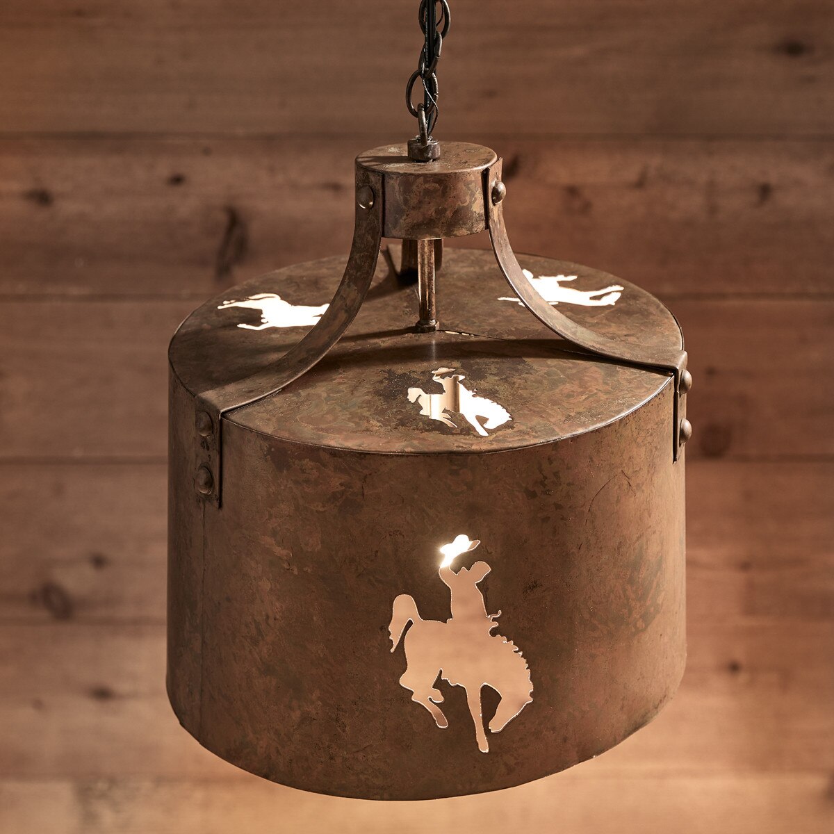 Decorative metal lantern with bucking horse designs on a wooden background