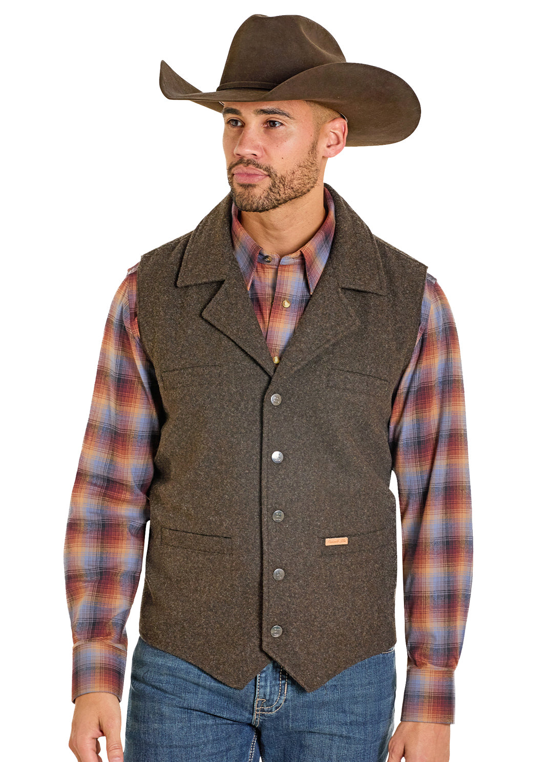 A man wearing a brown wool Panhandle Slim vest over a red and blue plaid shirt, blue jeans, and a brown cowboy hat, photographed against a plain white background.