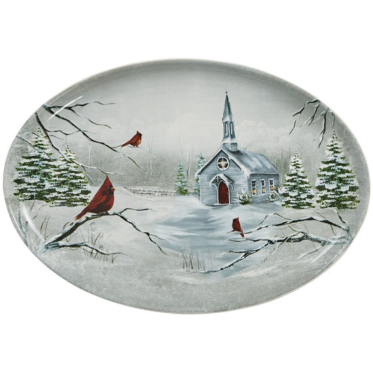 An oval decorative platter from Park Designs featuring a winter landscape scene with a small church, snow-covered evergreen trees, and red cardinals on branches, shown on a plain white background.