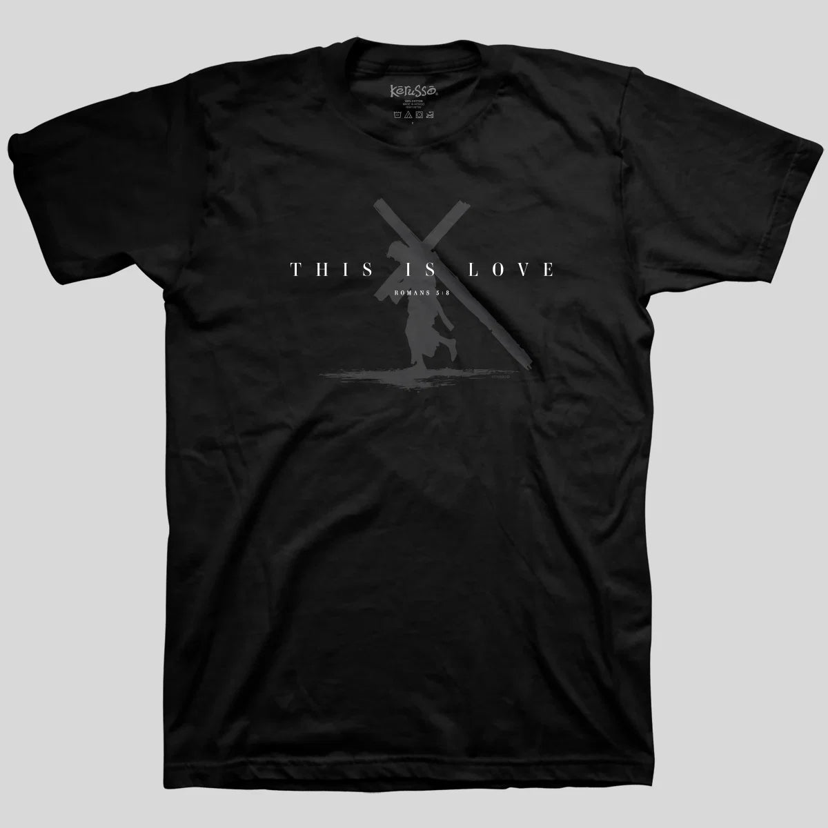 A black short-sleeve crewneck t-shirt from Kerusso with a dark gray graphic on the chest depicting a silhouette of Jesus carrying the cross, with the text 'THIS IS LOVE'  The shirt is displayed flat against a solid light gray background.
