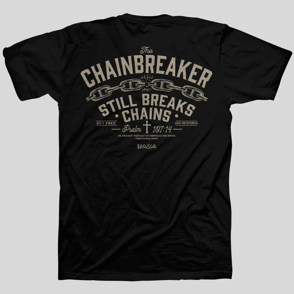 A black short-sleeve t-shirt from Kerusso shown from the back, featuring a distressed beige graphic print with the words 'The CHAINBREAKER STILL BREAKS CHAINS' and a chain motif, on a solid gray background.