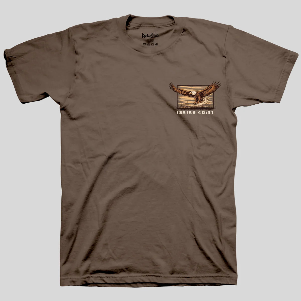 A brown short-sleeve crewneck t-shirt from Kerusso featuring a graphic of a bald eagle flying over a desert landscape with the text 'ISAIAH 40:31' printed below it, displayed on a solid gray background.