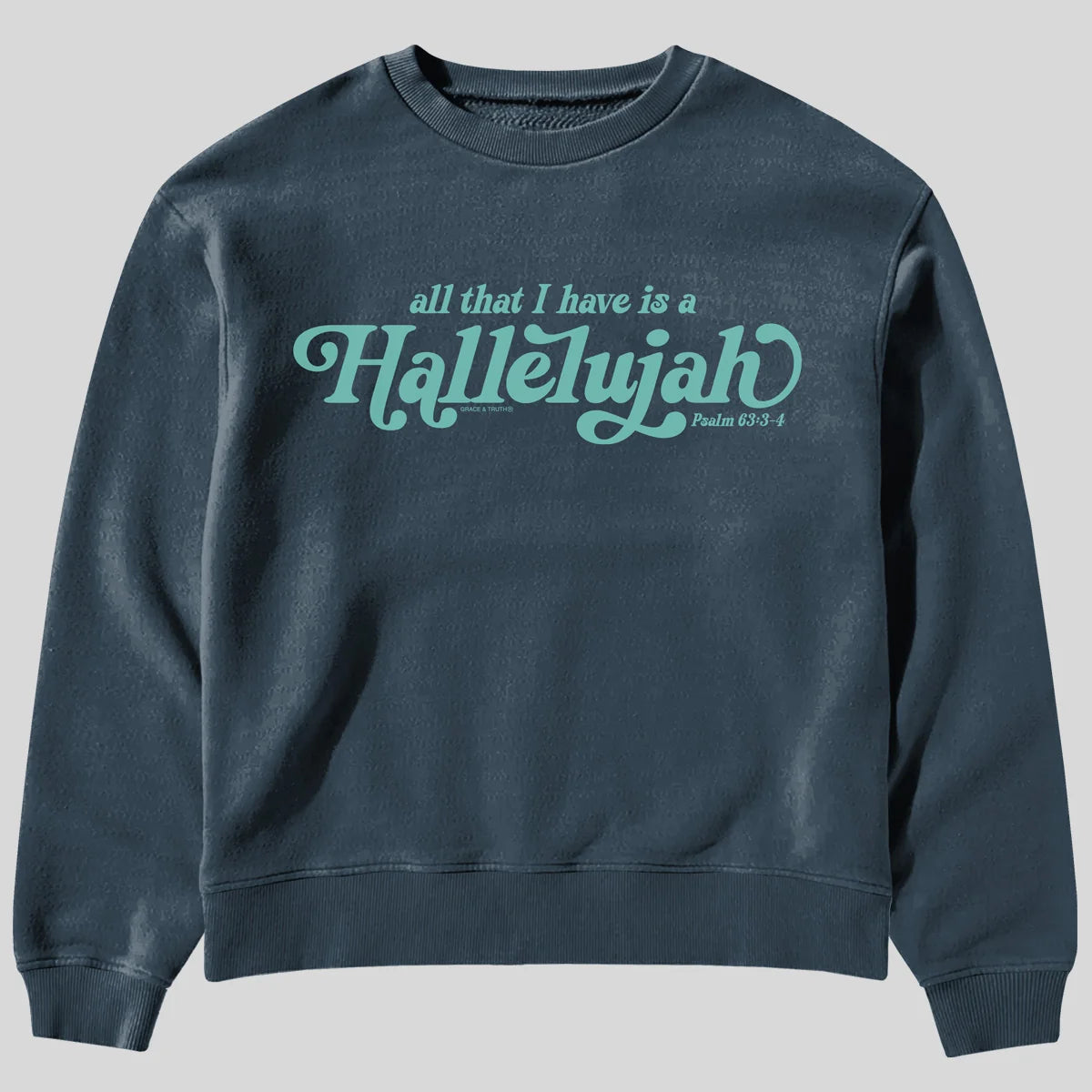 A dark slate blue crewneck sweatshirt from Kerusso featuring the text 'all that I have is a Hallelujah' and 'Psalm 63:3-4' printed in a light teal cursive font across the chest, displayed on a solid gray background.