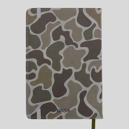 A hardcover notebook from Kerusso with a brown, gray, and beige camouflage pattern cover, featuring white elastic closure bands and a green ribbon bookmark.