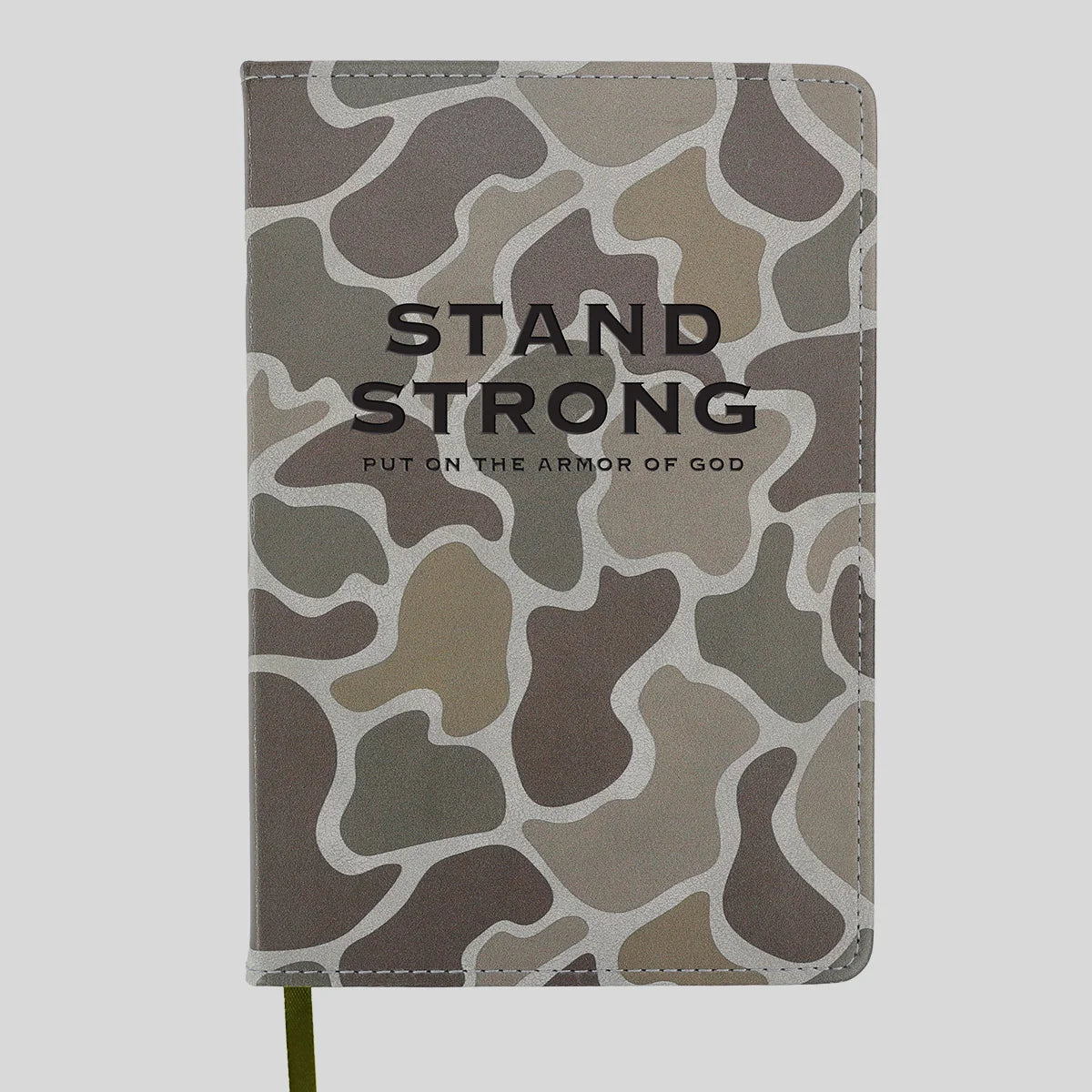 A hardcover notebook or journal from Kerusso featuring a muted camouflage pattern in shades of gray, brown, and beige, with the words 'STAND STRONG' and 'PUT ON THE ARMOR OF GOD' printed in black on the front cover.