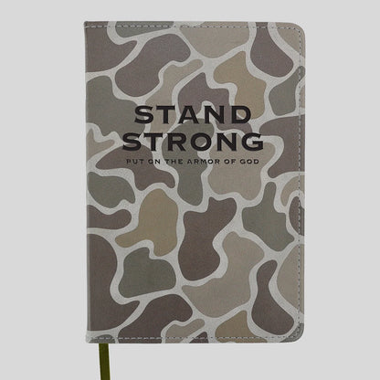 A hardcover notebook or journal from Kerusso featuring a muted camouflage pattern in shades of gray, brown, and beige, with the words 'STAND STRONG' and 'PUT ON THE ARMOR OF GOD' printed in black on the front cover.