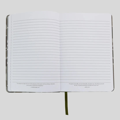 An open lined journal or notebook from Kerusso with blank white pages, small printed verses at the bottom of each page, and a dark olive bookmark ribbon hanging from the center, shown on a light gray background.