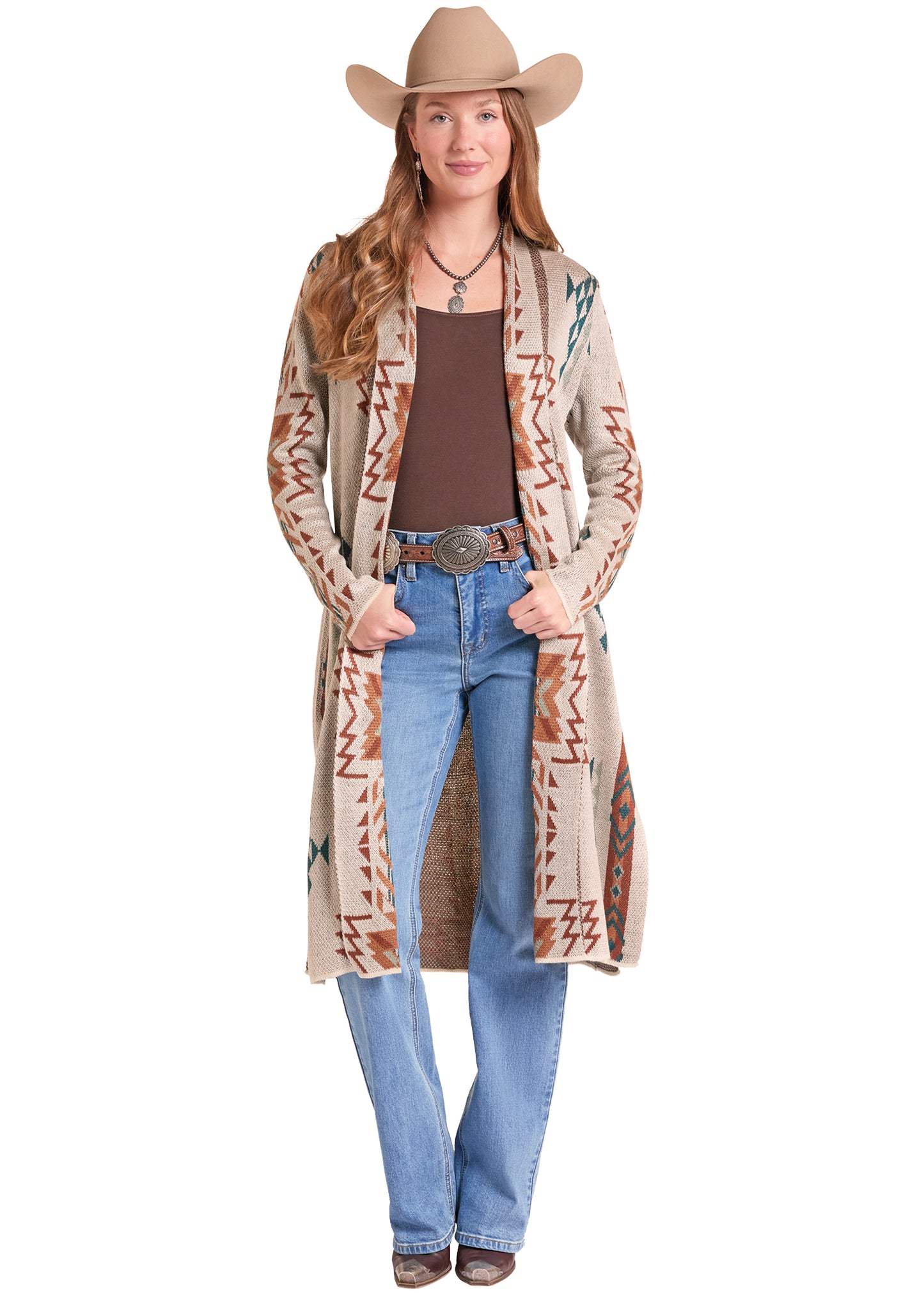 A woman modeling a long beige Rock&Roll Denim cardigan with brown, orange, and blue geometric patterns, styled with a brown tank top, blue jeans, a western belt, and a tan cowboy hat against a white background.