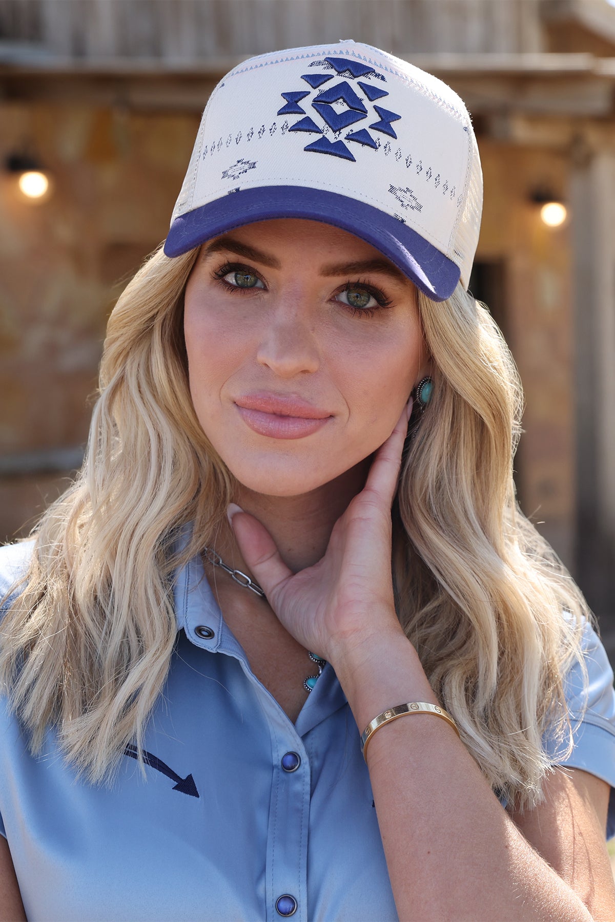 Woman wearing a white and navy cap by cruel denim with blue accents and a blue shirt, posing outdoors.