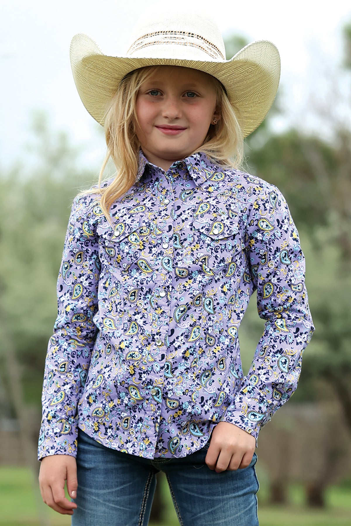 Young girl wearing a floral Cinch shirt and cowboy hat outdoors
