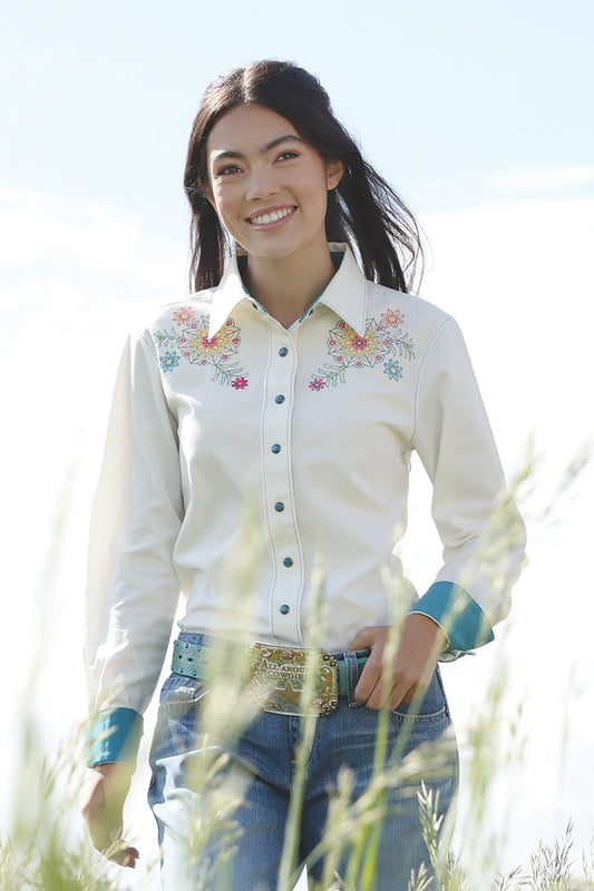 Woman wearing Cinch shirt with flowers on it and blue jeans and buckle in a field