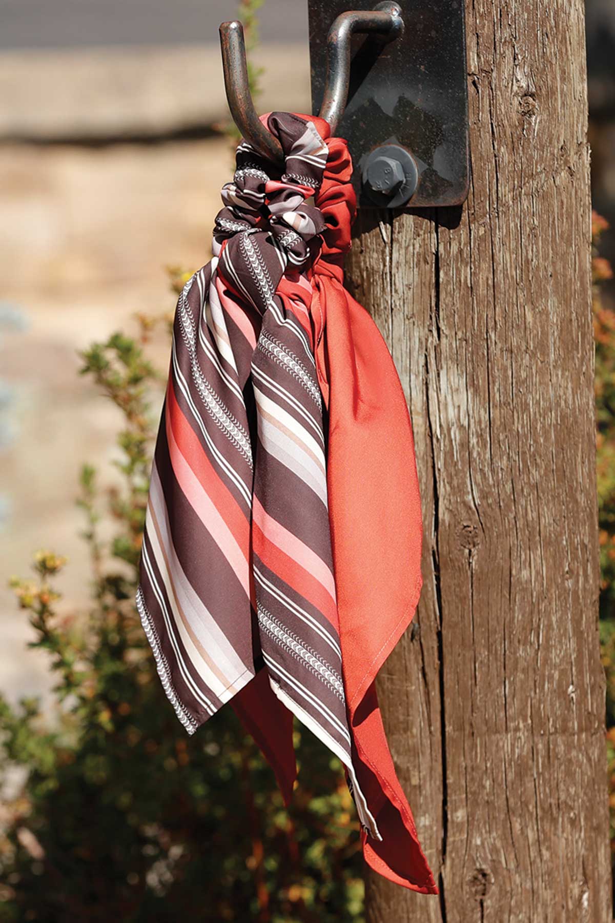 Set of scarf scrunchies from Cruel Denim in red and brown colors hanging on a post