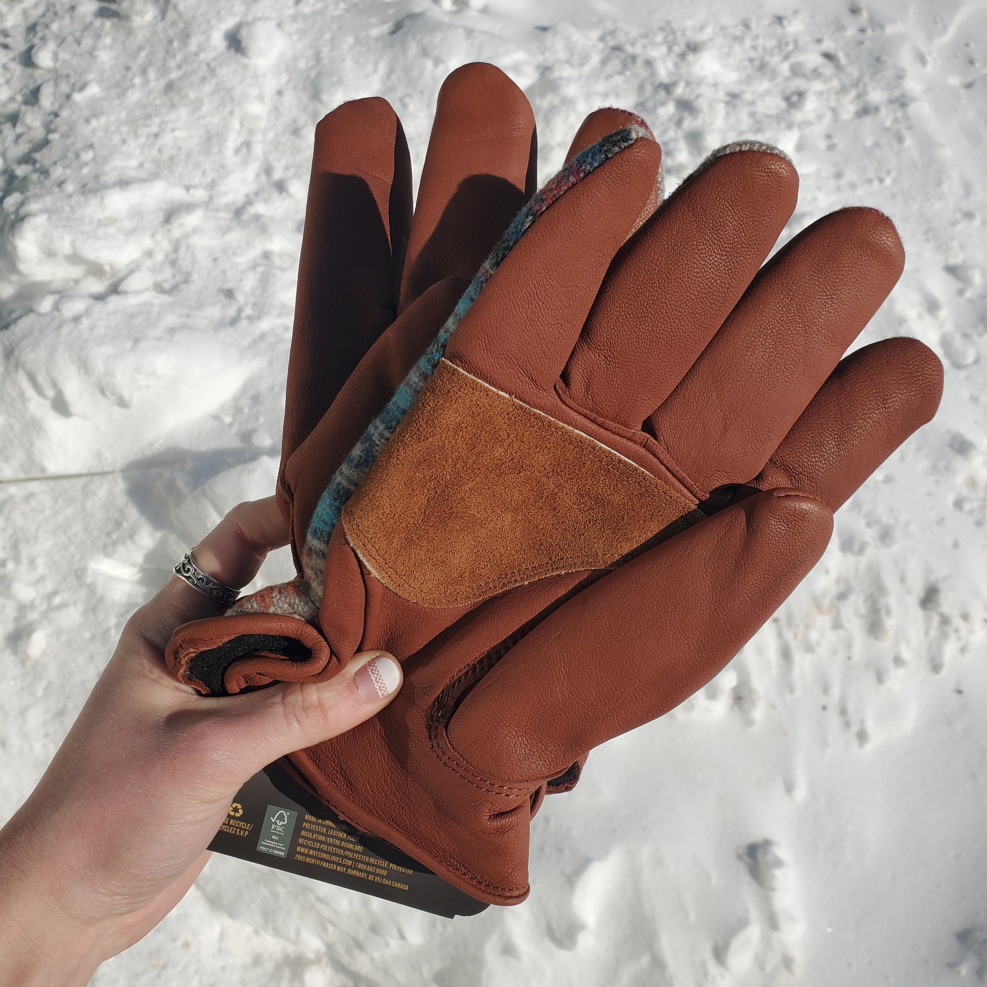 Brown leather gloves held against a snowy background