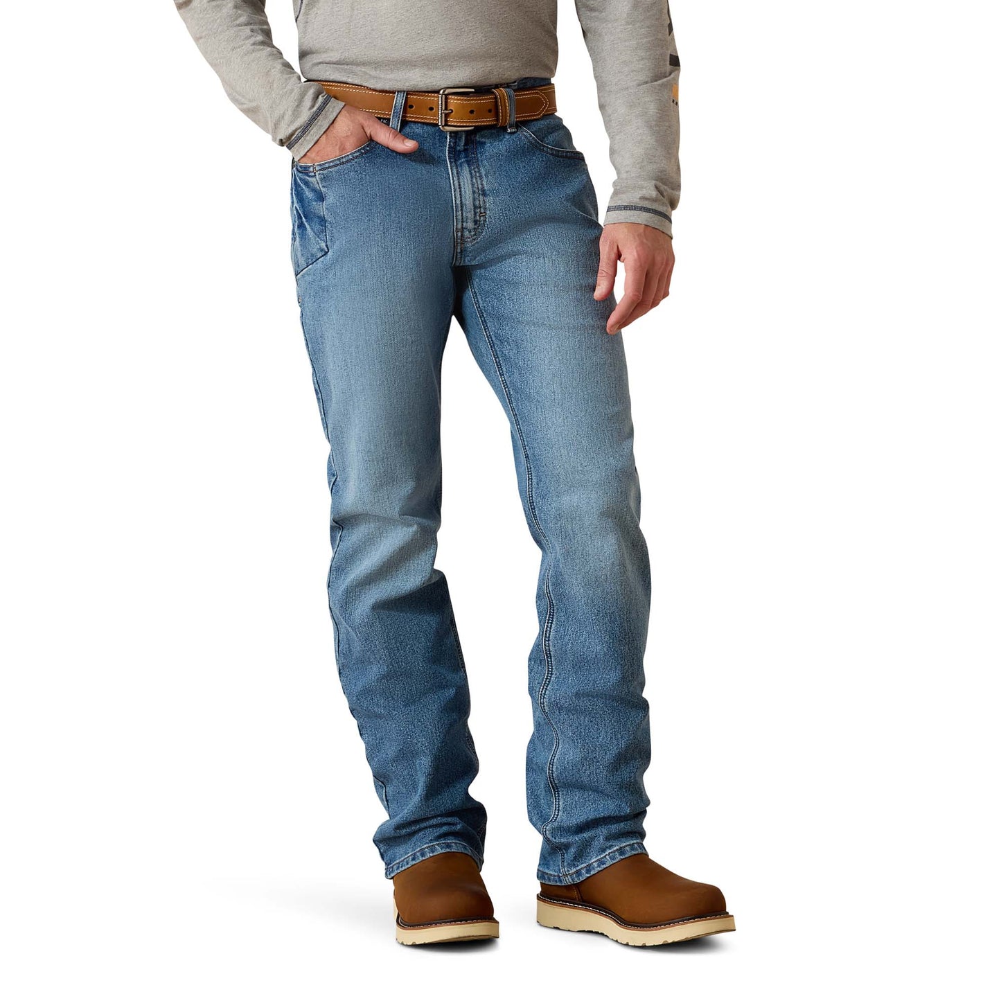 A man wearing blue hazed Ariat M4 Rebar DuraStretch Men's Jean with a mid-rise waist and boot cut, paired with a grey shirt and brown boots.