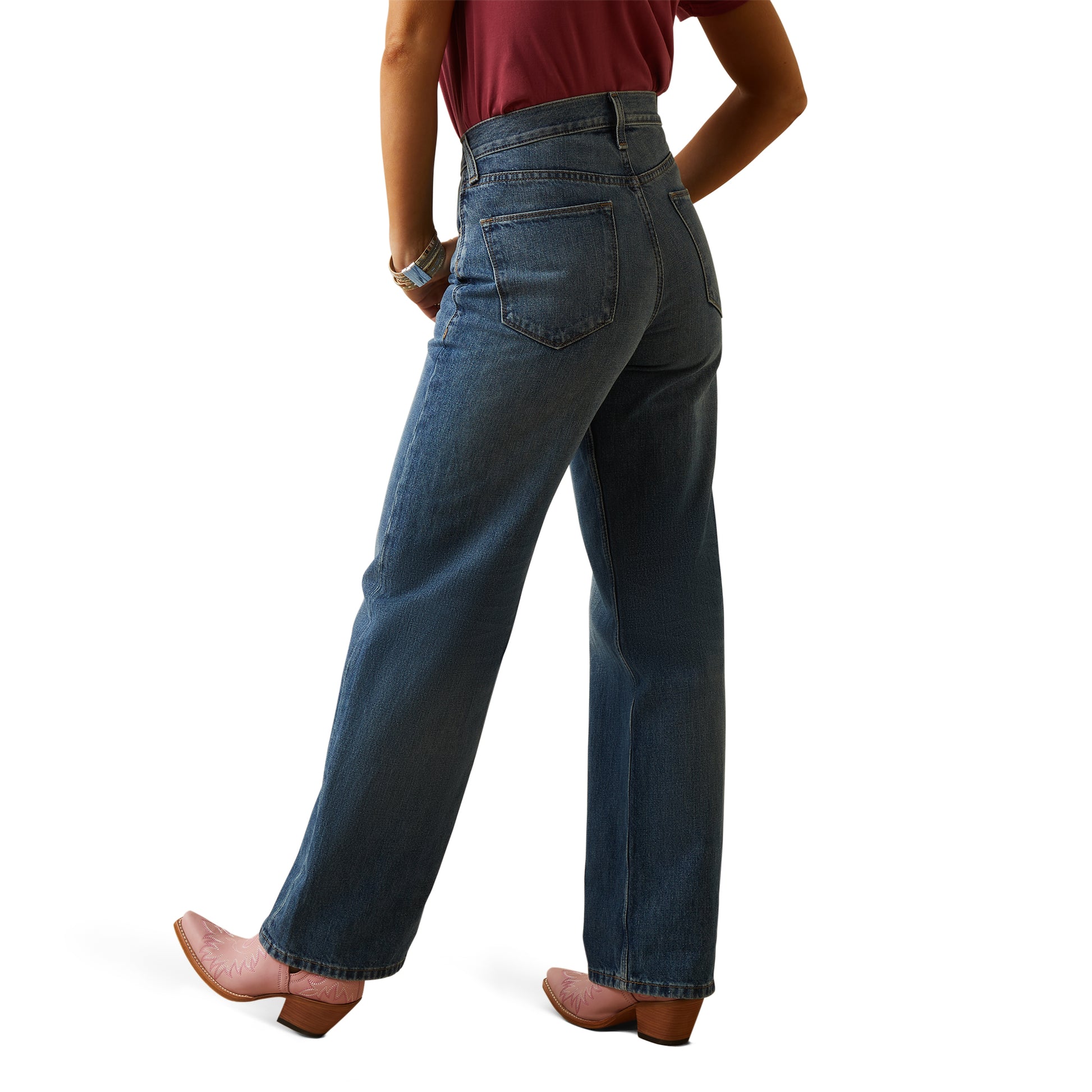 A woman is standing, wearing ultra high rise wide leg jeans and a belt with an animal pattern. She has accessories on her wrists and is posing against a white background.