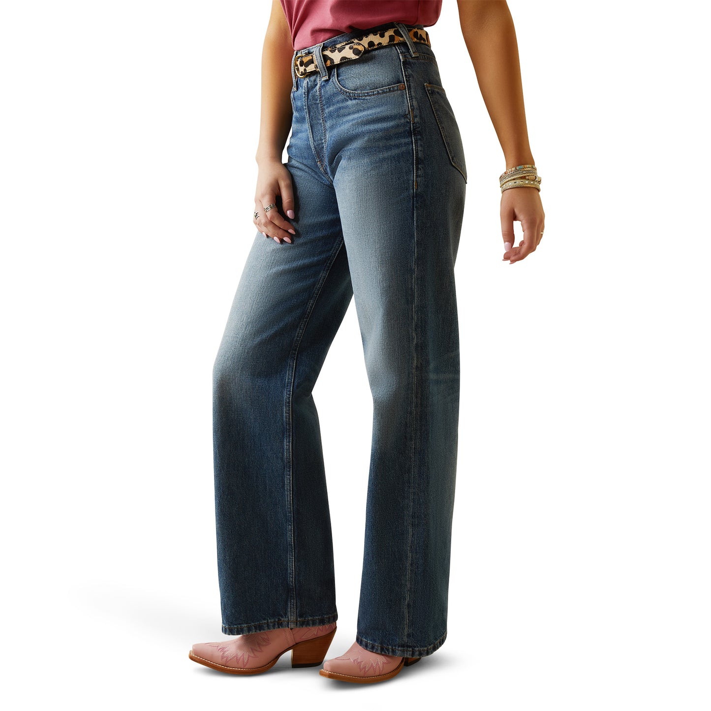 A woman is standing, wearing ultra high rise wide leg jeans and a belt with an animal pattern. She has accessories on her wrists and is posing against a white background.