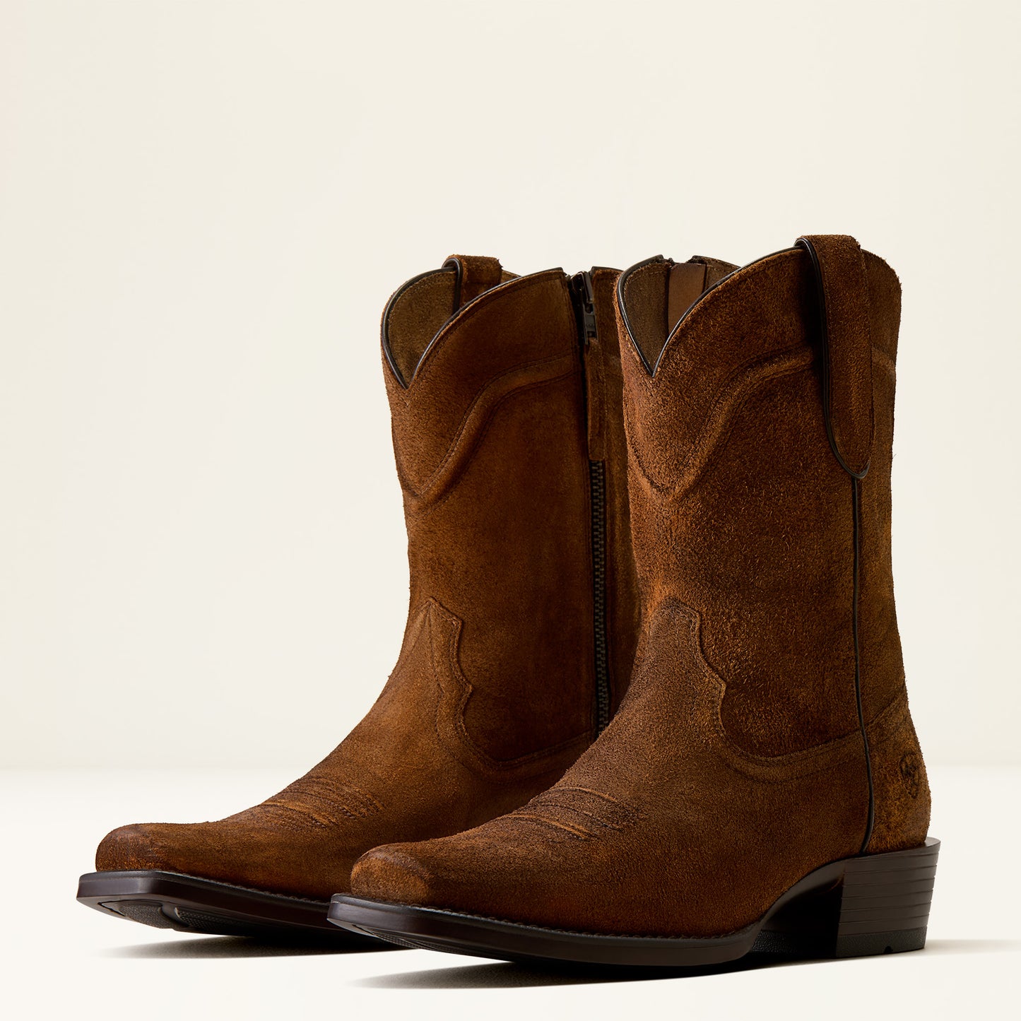 A pair of brown suede cowboy boots with side zippers, shown from a three-quarters angle against a clean, off-white background.
