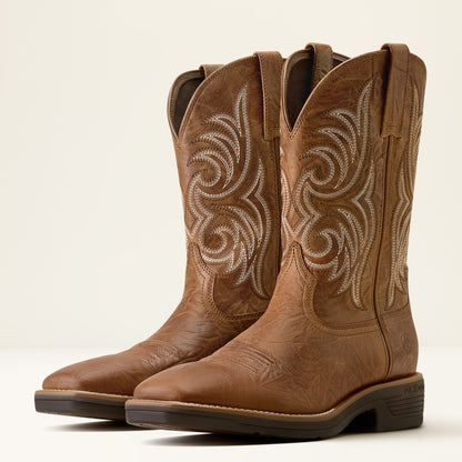 A pair of brown leather cowboy boots with white embroidered swirl patterns on the shafts, shown against a plain light beige background.