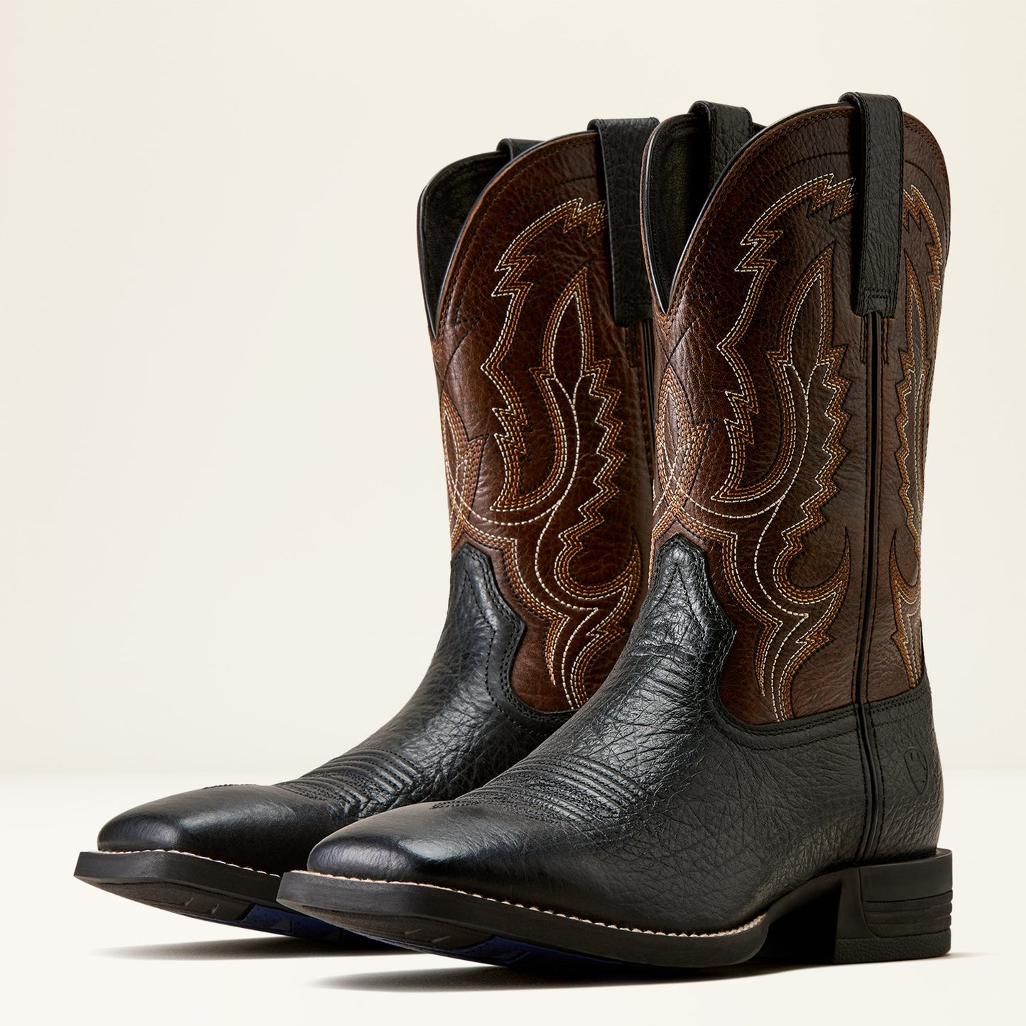 a pair of brown and black wide square toe ariat boots on a cream background