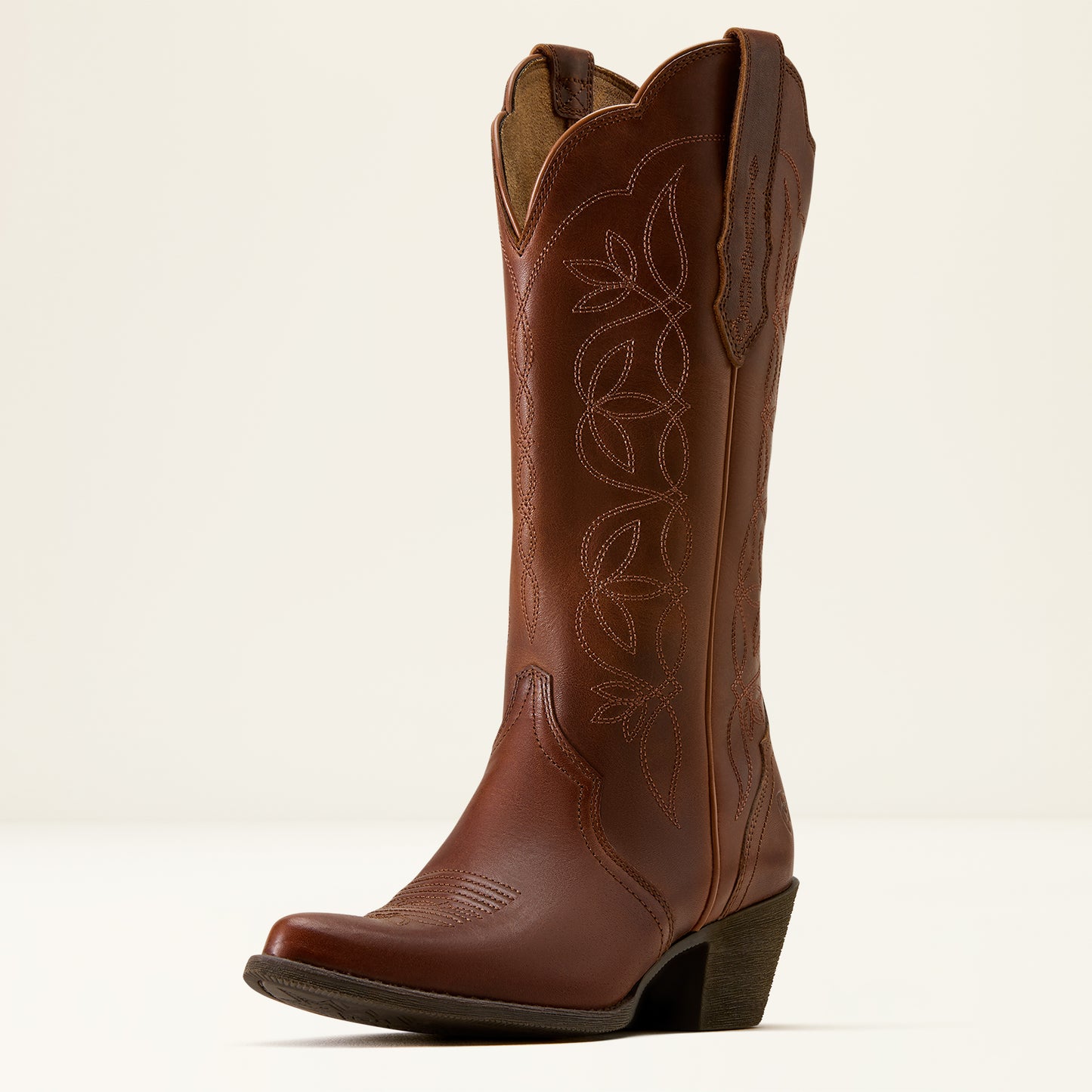 A single brown leather cowboy boot with decorative floral stitching on the shaft, a pointed toe, and a low block heel, photographed against a clean off-white background.