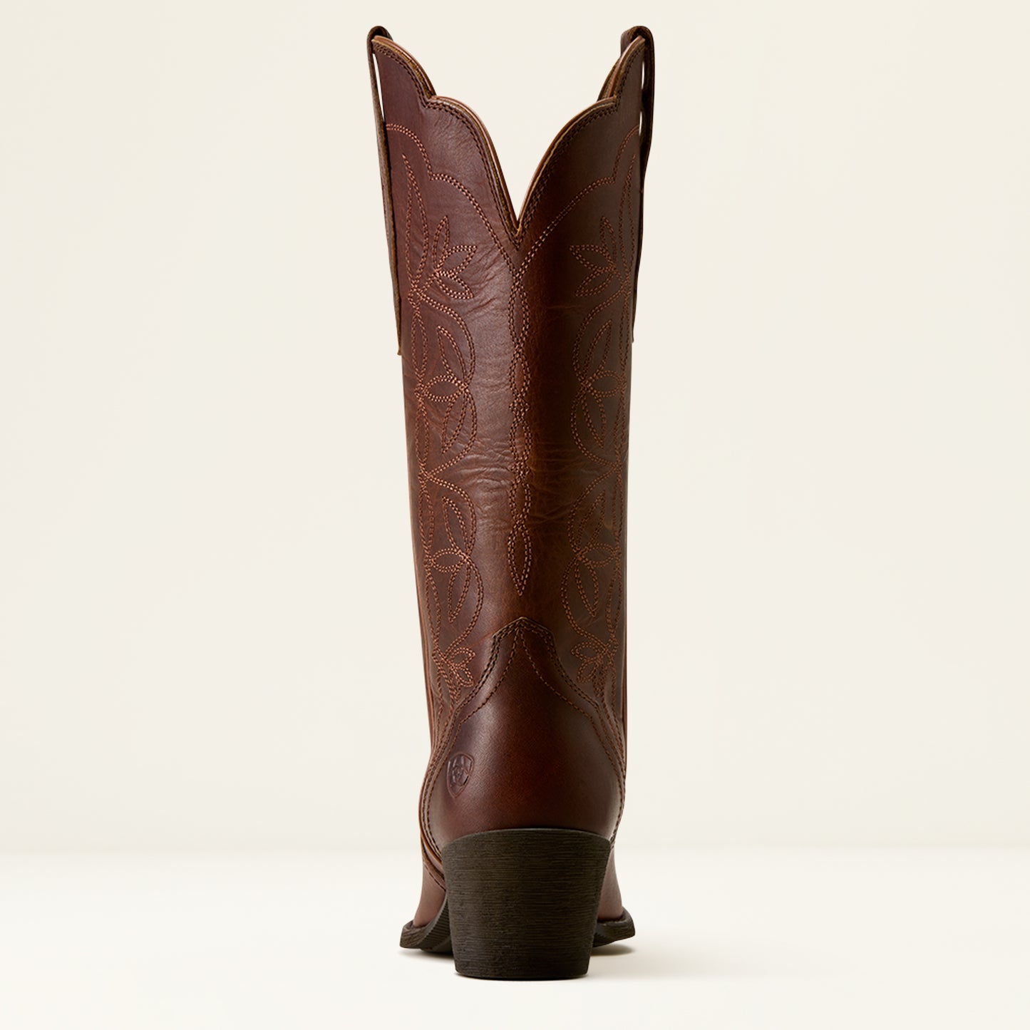 A single brown leather cowboy boot shown from the back, featuring decorative tooling and stitching on the shaft, set against a plain off-white background.