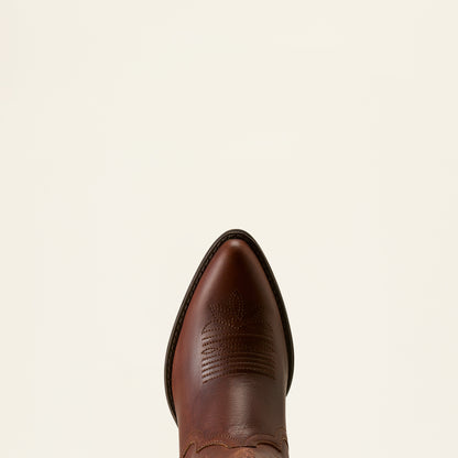 A close-up top-down view of a brown leather cowboy boot toe, showing the pointed tip and decorative stitching, set against a solid off-white background.