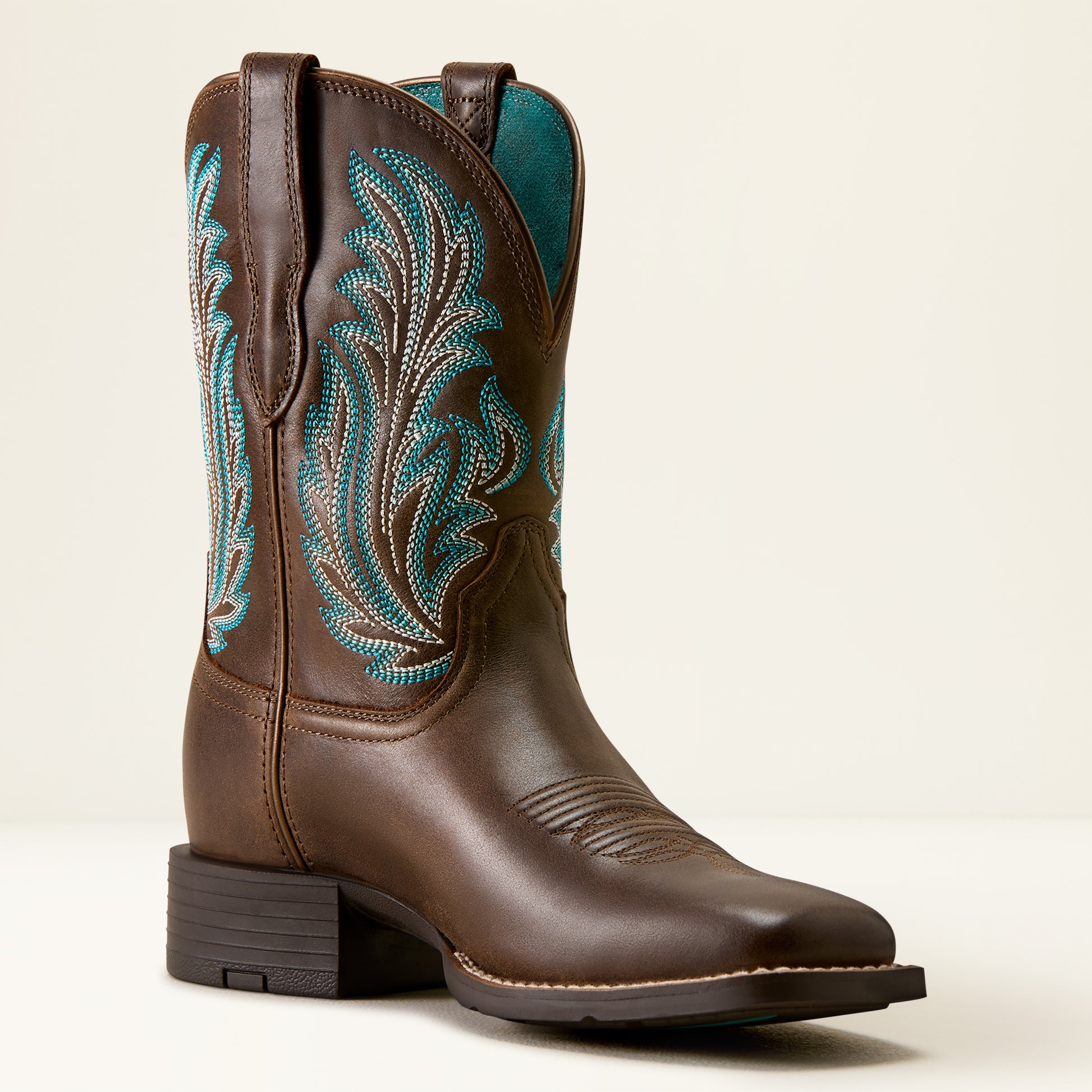 A single brown leather cowboy boot with turquoise and white embroidered leaf patterns on the shaft, set against a plain light beige background.