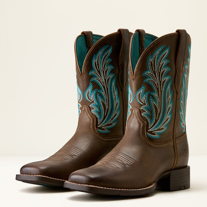 A pair of brown leather cowboy boots with turquoise and white embroidered floral patterns on the shafts, shown against a plain light beige background.
