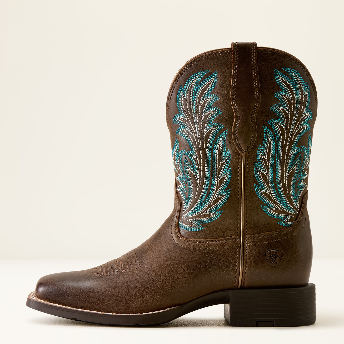 A brown leather cowboy boot with turquoise and white embroidered leaf patterns on the shaft, shown in a side profile against a light beige background.