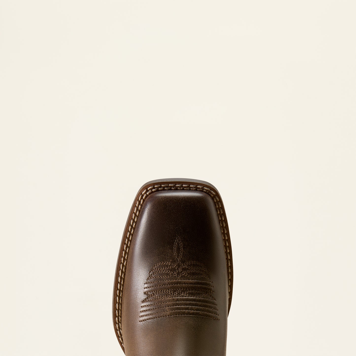 Close-up of the toe of a dark brown leather cowboy boot with decorative stitching, shown against a solid off-white background.