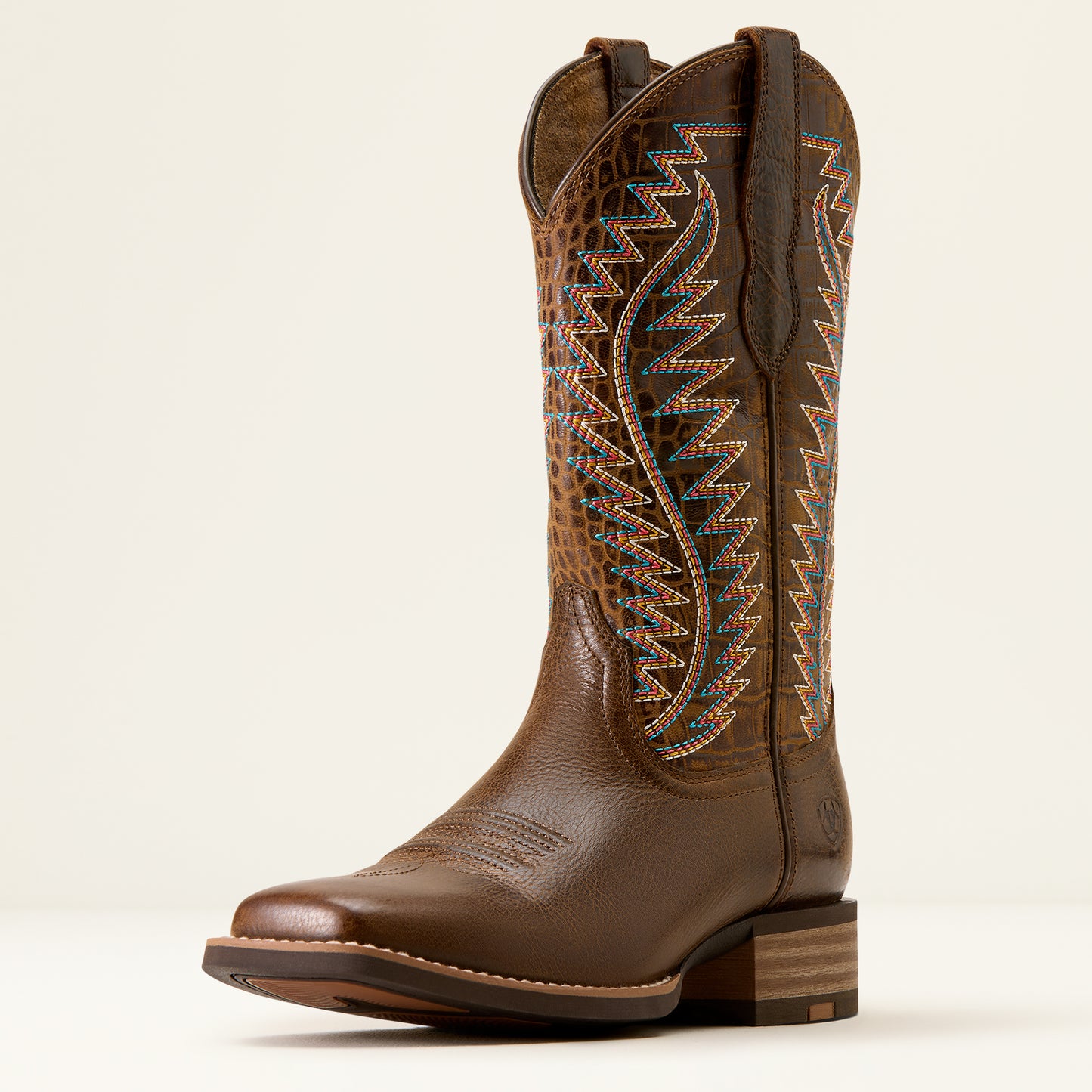 A brown leather cowboy boot with a textured alligator-pattern shaft, colorful geometric embroidery, and a stacked wood-look heel, shown against a plain light background.